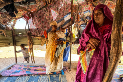 Kobieta w tradycyjnym stroju farbuje bawełniany szal w trudnych warunkach życiowych, jej młodszy syn choruje obok